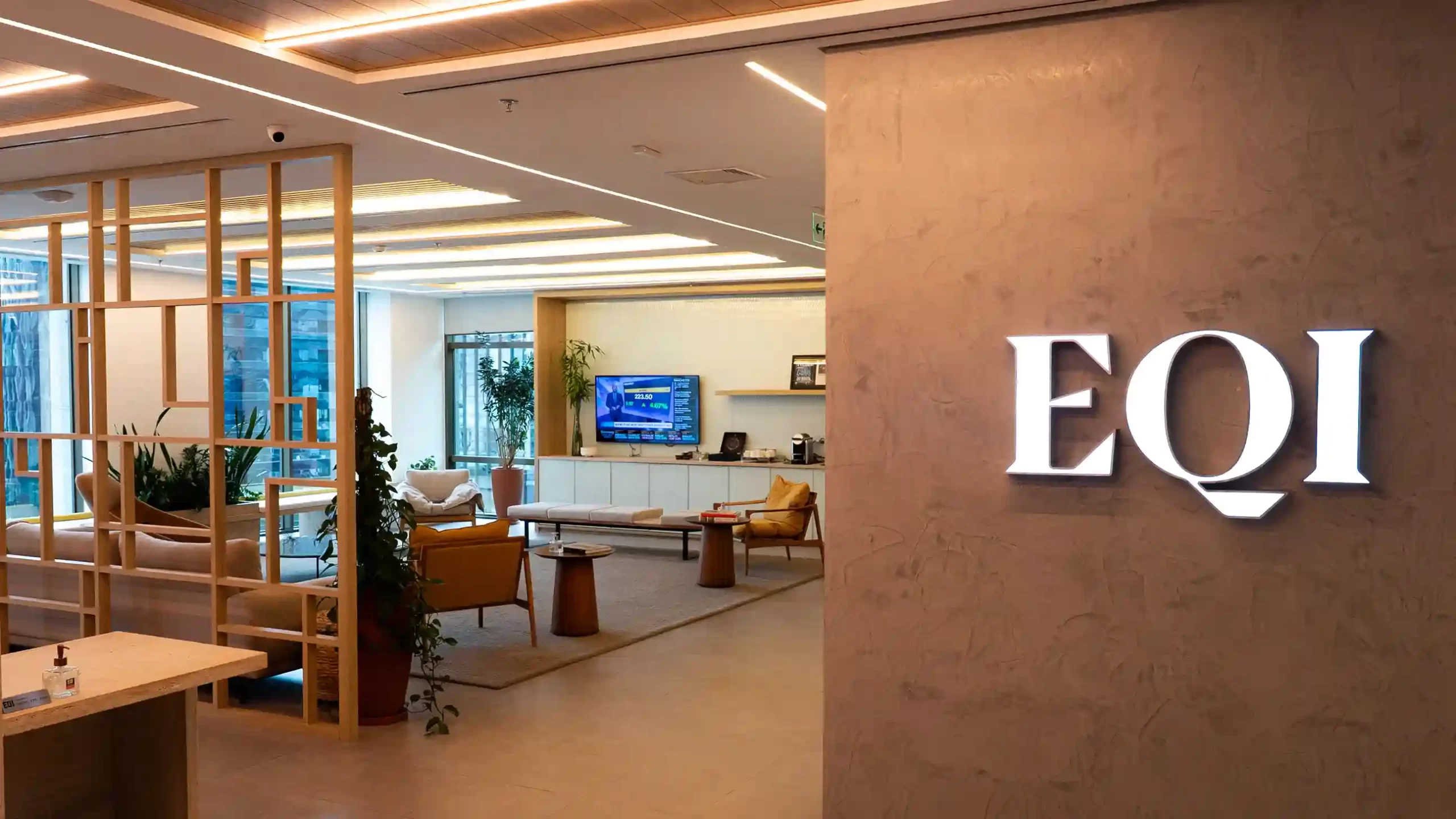 Sala de reuniões moderna e elegante da EQI, com o logotipo em uma parede de pedra, simbolizando o encontro sobre as mudanças tributárias e planejamento patrimonial.