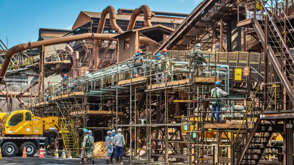 Vista de trabalhadores em um canteiro de obras complexo dentro de uma siderúrgica (provavelmente a Usiminas), representando a transação de controle pela Ternium.