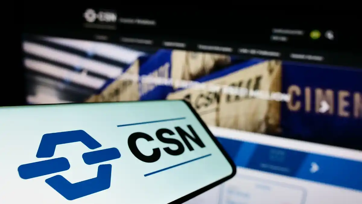 O logotipo da CSN (Companhia Siderúrgica Nacional) em um smartphone, com imagens de minério e cimento desfocadas ao fundo, representando o balanço do 3º trimestre de 2025.