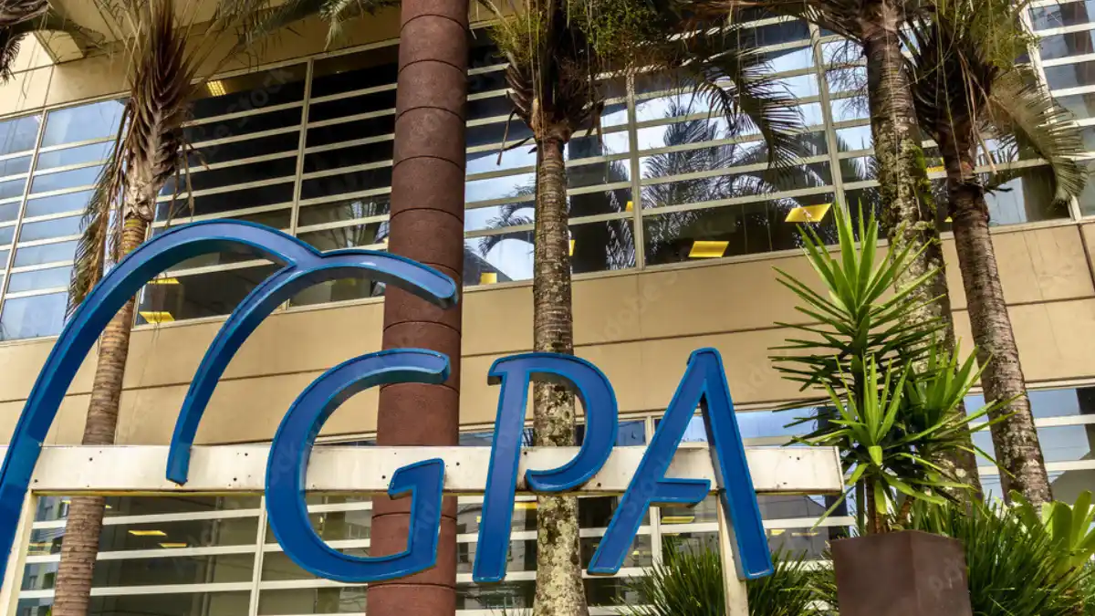 O logotipo em azul do GPA (Grupo Pão de Açúcar) na fachada de um prédio, com palmeiras ao fundo, simbolizando a reversão do prejuízo no 3º trimestre de 2025.
