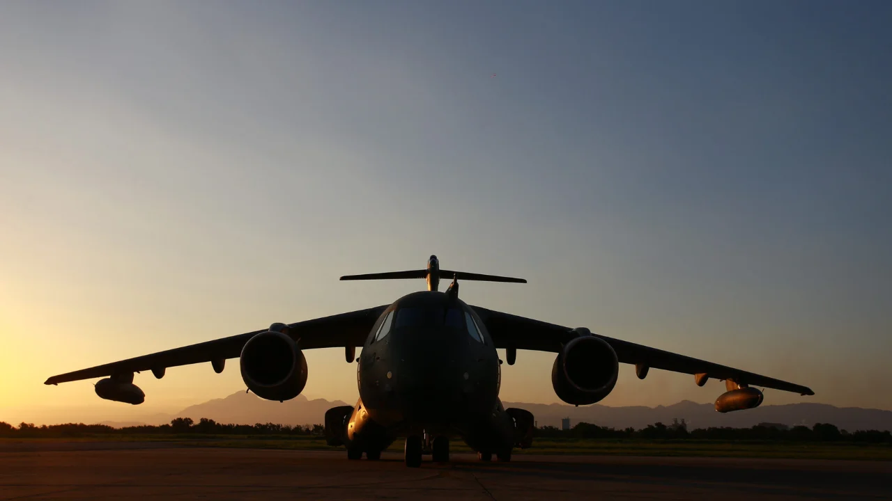 Aeronave militar C-390 Millennium da Embraer vista de frente na pista de pouso ao pôr do sol.