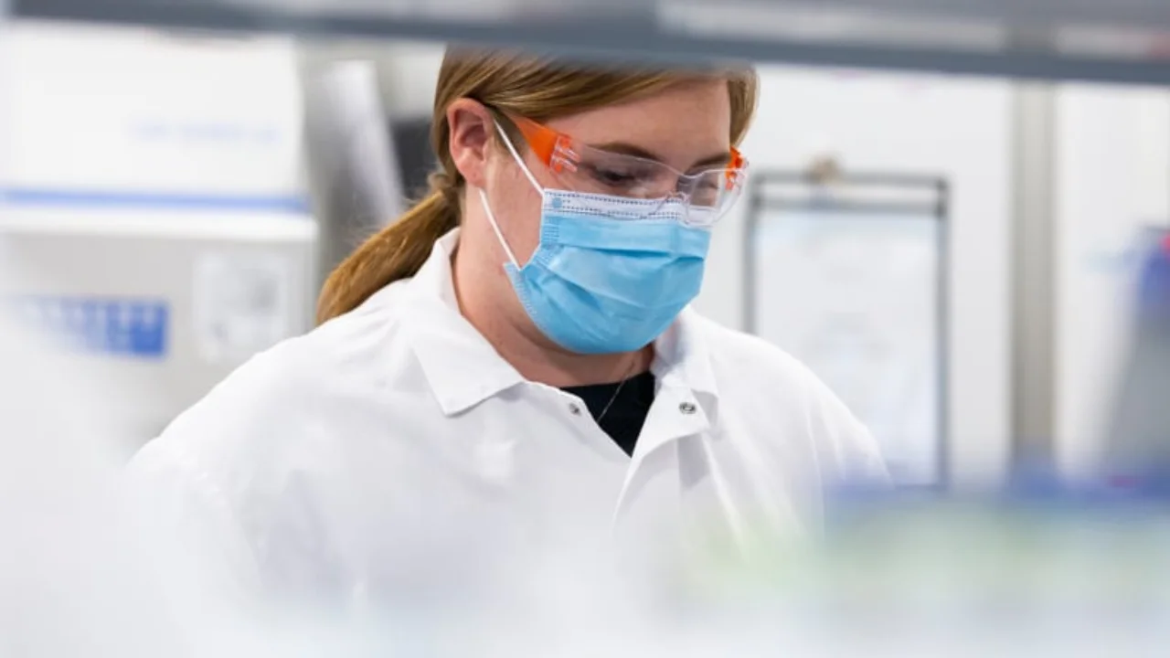Pesquisadora de jaleco e óculos de proteção em laboratório da Moderna desenvolvendo vacina de mRNA contra melanoma.