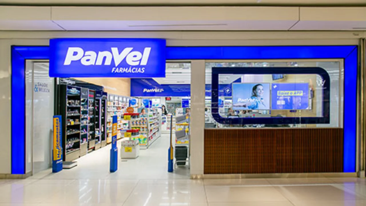 Fachada de loja da Panvel Farmácias em shopping center com moldura iluminada em azul vibrante, tela digital promovendo o aplicativo da marca e interior exibindo prateleiras de medicamentos e produtos de beleza.