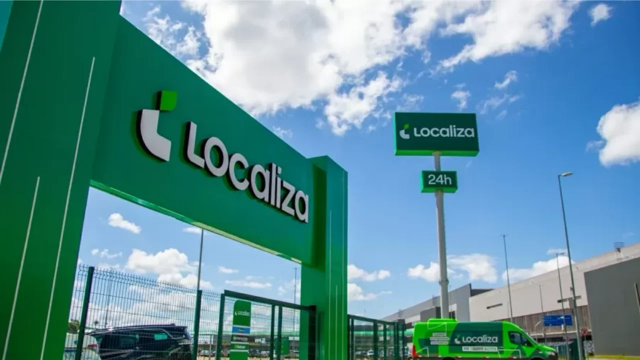 Fachada verde de uma agência de aluguel de carros da Localiza sob céu ensolarado.