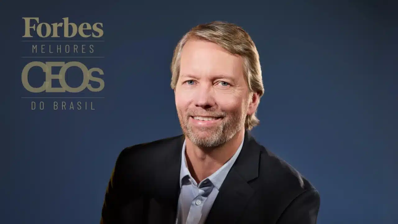 Retrato corporativo de executivo usando terno escuro e camisa clara, posicionado diante de fundo azul. À esquerda, aparece o selo "Forbes Melhores CEOs do Brasil"